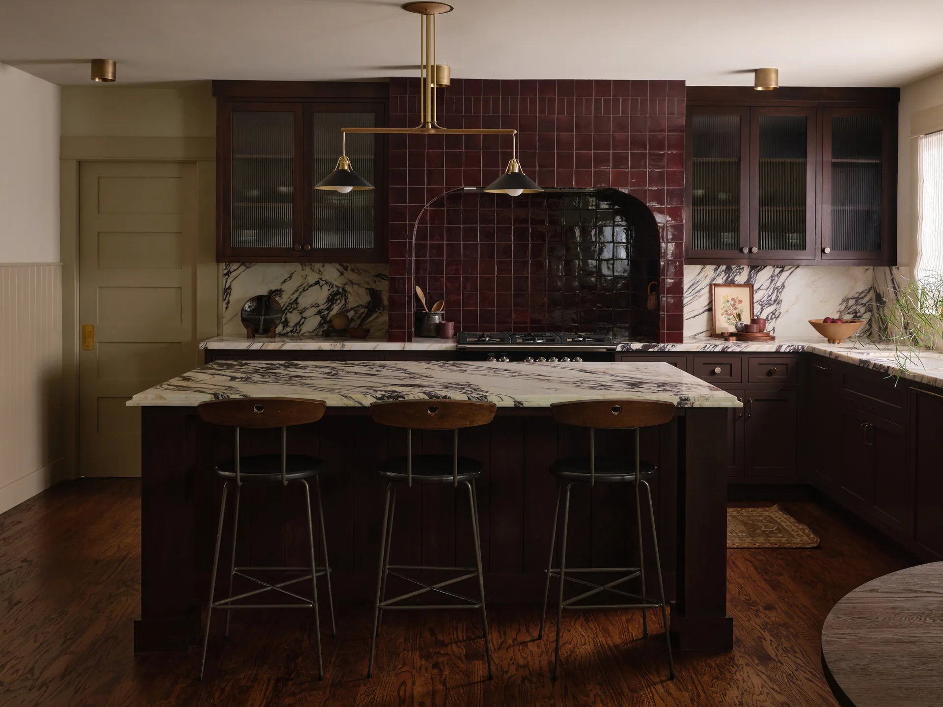 Craftsman kitchen with dark cabinetry, Calacatta Viola marble island, and burgundy tile range alcove