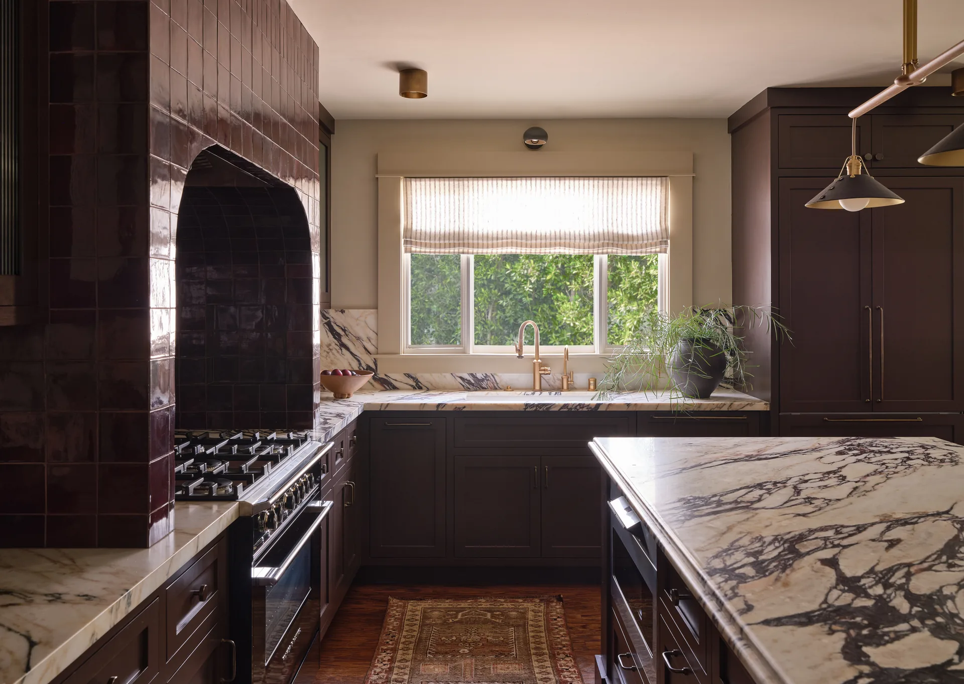 Kitchen view toward the window with marble counters and dark painted cabinets