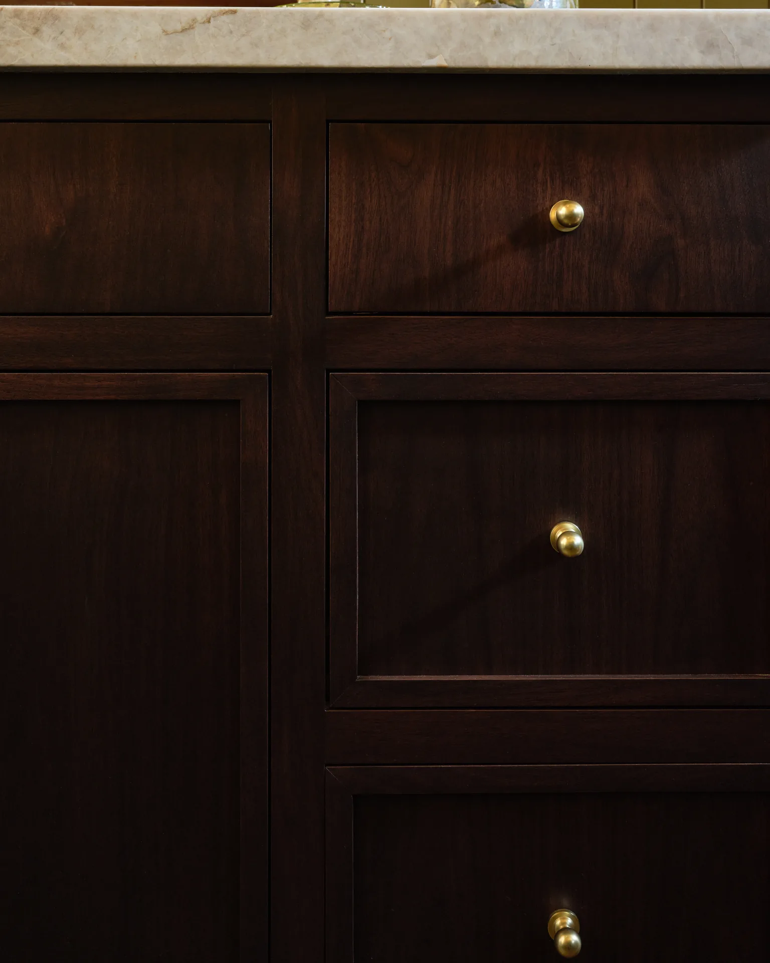 Detail of stained wood cabinet drawers with brass knobs