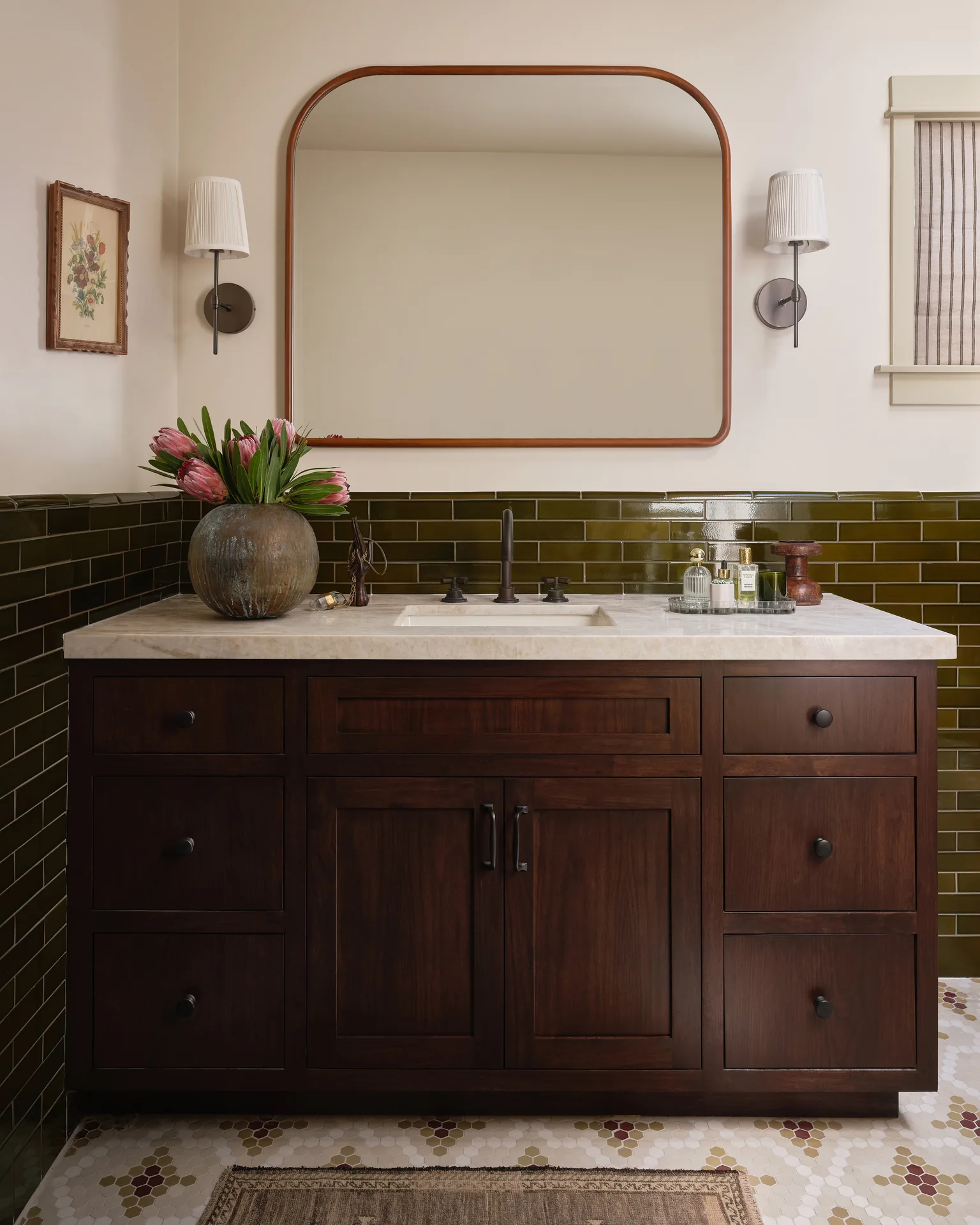 Main bathroom with olive subway tile, stained wood vanity, and arched mirror